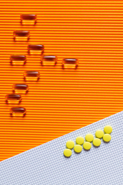 flat lay of yellow pills on and jelly capsules on white and orange textured background - Foto, imagen
