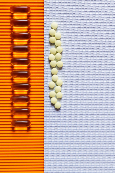 vlakke lay-out van rijen met gele pillen op en gelei capsules op witte en oranje textuur achtergrond - Foto, afbeelding