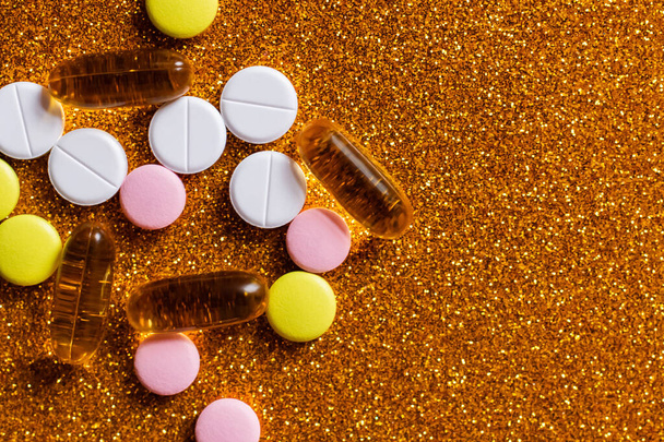 vista superior de diferentes pílulas coloridas e cápsulas em fundo dourado brilhante - Foto, Imagem