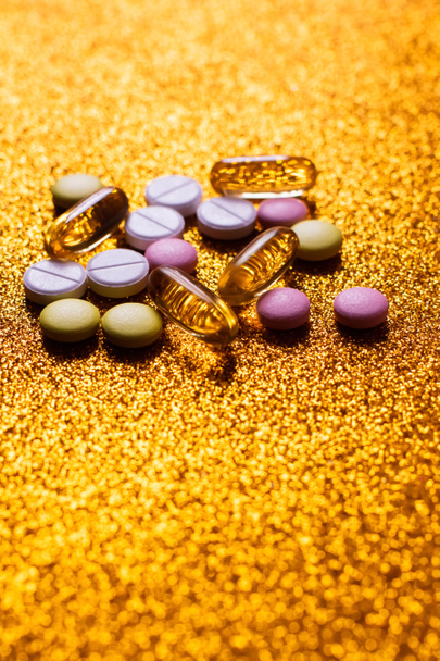 diferentes píldoras y cápsulas de colores sobre fondo dorado brillante - Foto, imagen