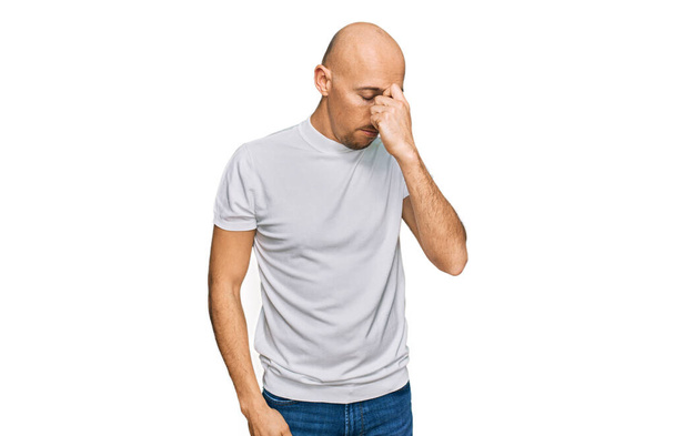 Bald man with beard wearing casual white t shirt tired rubbing nose and eyes feeling fatigue and headache. stress and frustration concept.  - Photo, Image