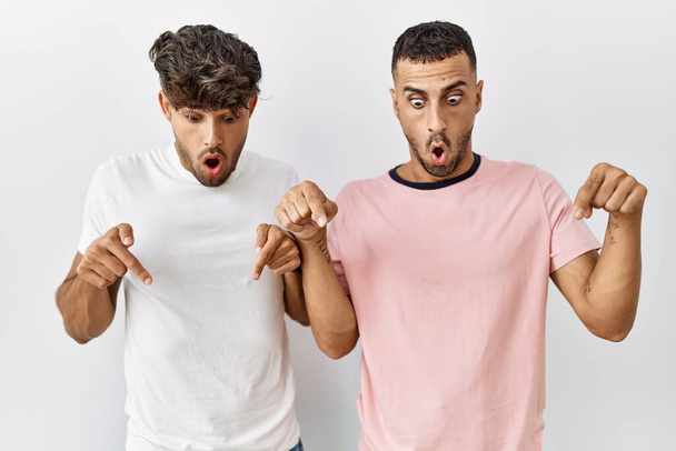 Nuori homo pari seisoo yli eristetty tausta osoittaa alas sormet näyttää mainos, yllättynyt kasvot ja avoin suu  - Valokuva, kuva
