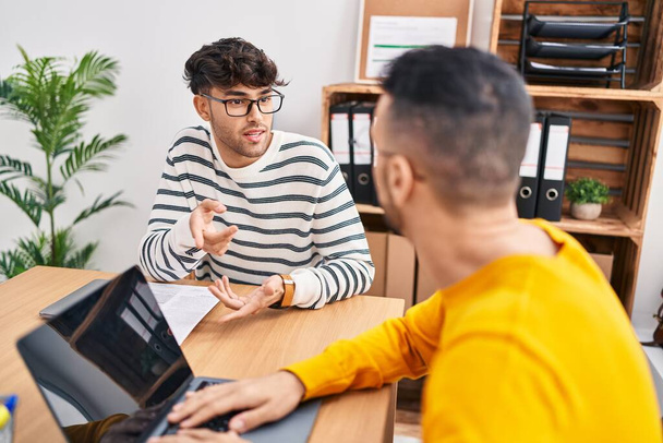 Δύο εργαζόμενοι στις επιχειρήσεις χρησιμοποιώντας φορητό υπολογιστή μιλώντας στο γραφείο - Φωτογραφία, εικόνα