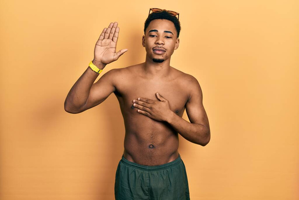 Young african american man wearing swimwear and swimmer glasses swearing with hand on chest and open palm, making a loyalty promise oath  - Фото, зображення