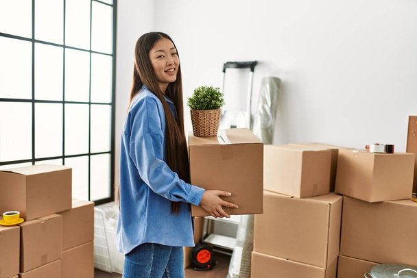Молодая китайская девушка улыбается счастливо держа картонную коробку в новом доме - Фото, изображение
