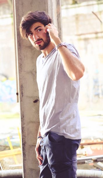 handsome dark-haired italian guy in decadent abandoned factory uses the phone. High quality photo - Photo, Image