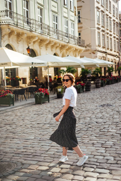 Summer fashion, white t-shirt and polka-dot skirt. Beautiful girl in summertime outfit walks on old city square - Φωτογραφία, εικόνα