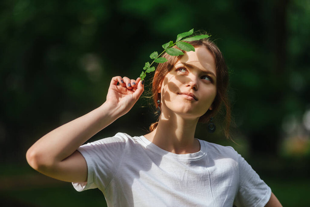 Girl holds a branch with leaves in her hand. Young woman summer portrait on natural green background - Foto, Imagen