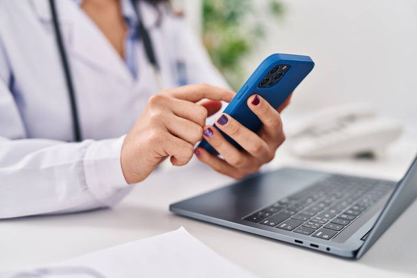 Fiatal spanyol nő visel orvos egyenruha smartphone dolgozik a klinikán - Fotó, kép