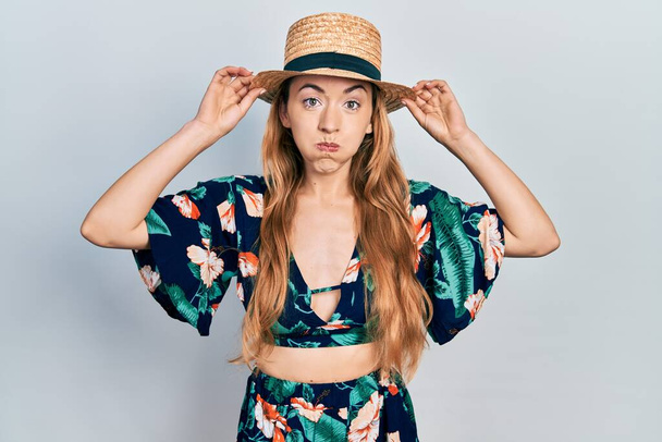 Jeune femme caucasienne portant un chapeau d'été gonflant les joues avec un visage drôle. bouche gonflée d'air, attrapant l'air.  - Photo, image