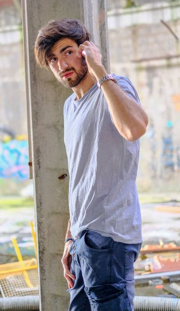 handsome dark-haired italian guy in decadent abandoned factory uses the phone. High quality photo - Фото, зображення
