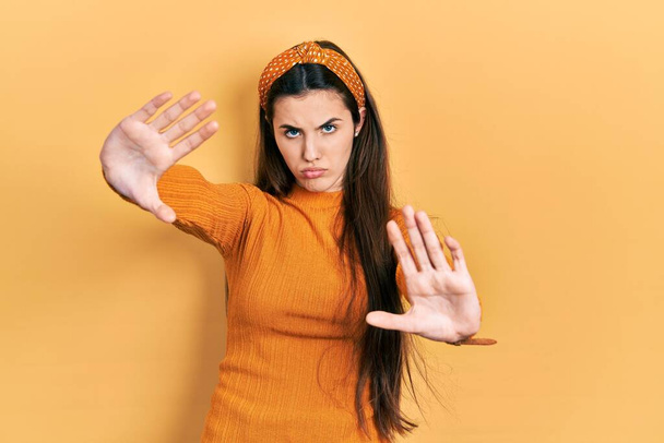 Giovane adolescente bruna che indossa maglione giallo casual facendo cornice con mani palme e dita, prospettiva fotocamera  - Foto, immagini