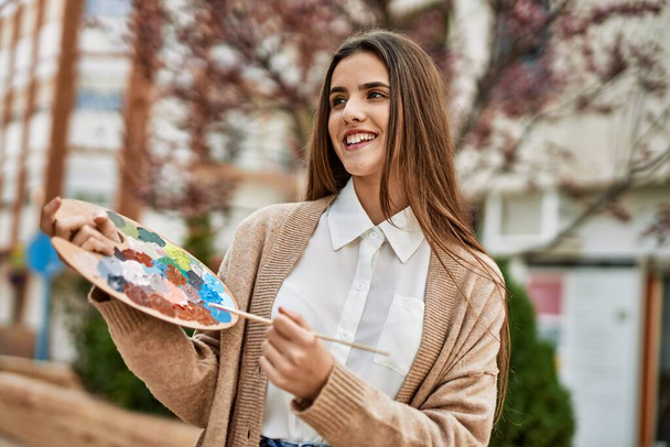 Молодая латиноамериканская художница улыбается счастливой картине в городе. - Фото, изображение