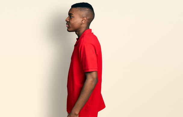 Nuori afrikkalainen amerikkalainen mies päällään rento punainen t-paita etsii sivuun, rentoutua profiilin poseeraa luonnolliset kasvot ja luottavainen hymy.  - Valokuva, kuva