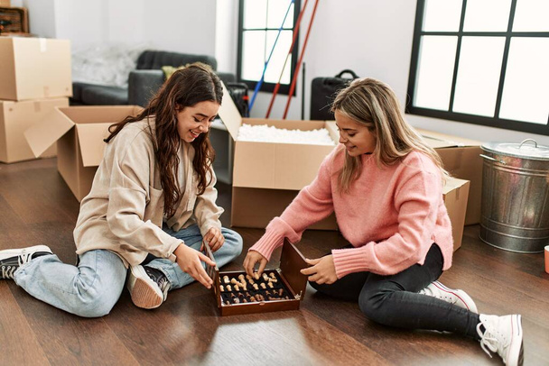 Молода пара посміхається щаслива гра в шахи, сидячи на підлозі в новому будинку
. - Фото, зображення