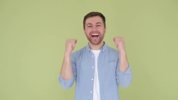 Handsome young man rejoices, raising his arms, feeling victory, close up, on green background - Footage, Video