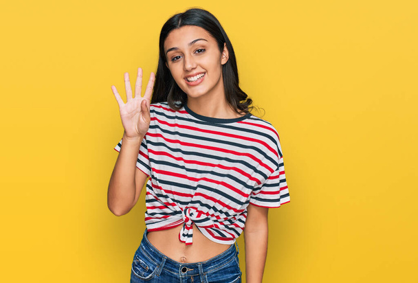 Jeune fille hispanique portant des vêtements décontractés montrant et pointant vers le haut avec les doigts numéro quatre tout en souriant confiant et heureux.  - Photo, image