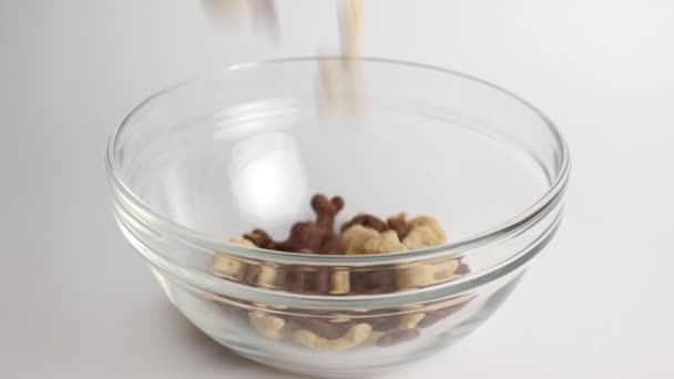 Granola is poured into a transparent bowl on a white background. Healthy food. Baby food. - Filmagem, Vídeo