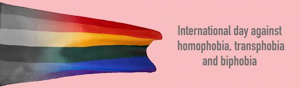 una bandera del orgullo del arco iris y el texto del día internacional contra la homofobia, la transfobia y la bifobia sobre un fondo rosa, en un formato panorámico para utilizar como banner web - Foto, Imagen