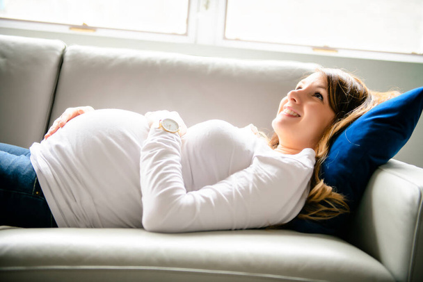 A happy pregnant woman lying on sofa at home - Fotoğraf, Görsel