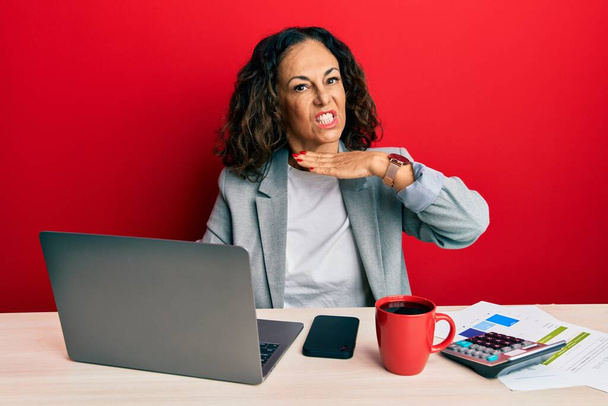 Beautiful middle age woman working at the office drinking a cup of coffee cutting throat with hand as knife, threaten aggression with furious violence  - Fotoğraf, Görsel