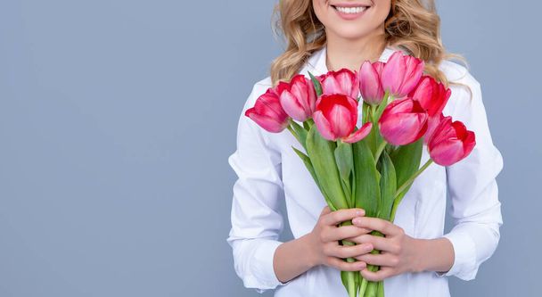 positive blond woman with spring tulip flowers on grey background - Фото, изображение