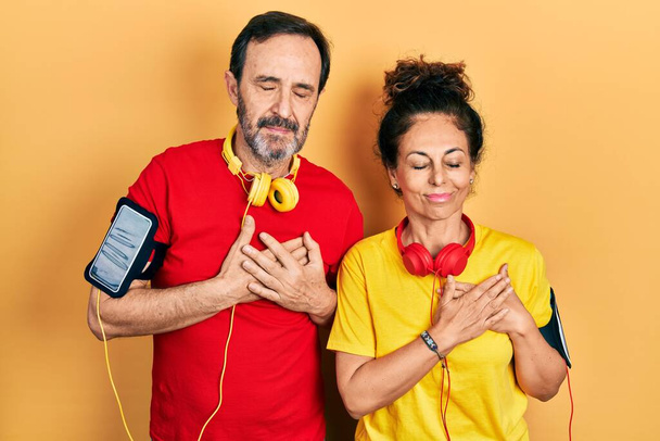 Middle age couple of hispanic woman and man wearing sportswear and arm band smiling with hands on chest with closed eyes and grateful gesture on face. health concept.  - Photo, image
