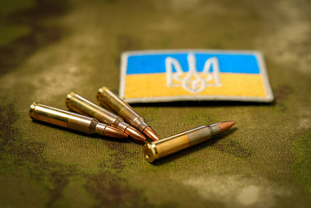 Patch με τη σημαία και το παλτό των όπλων της Ουκρανίας, φυσίγγια τουφέκι σε φόντο καμουφλάζ. - Φωτογραφία, εικόνα