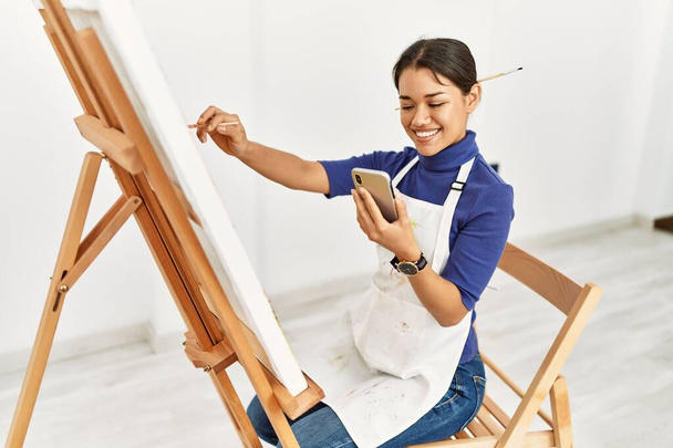 Молодая латиноамериканка использует рисунок на смартфоне в арт-студии - Фото, изображение