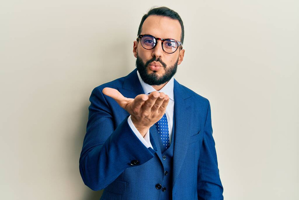 Young man with beard wearing business suit and tie looking at the camera blowing a kiss with hand on air being lovely and sexy. love expression.  - Zdjęcie, obraz
