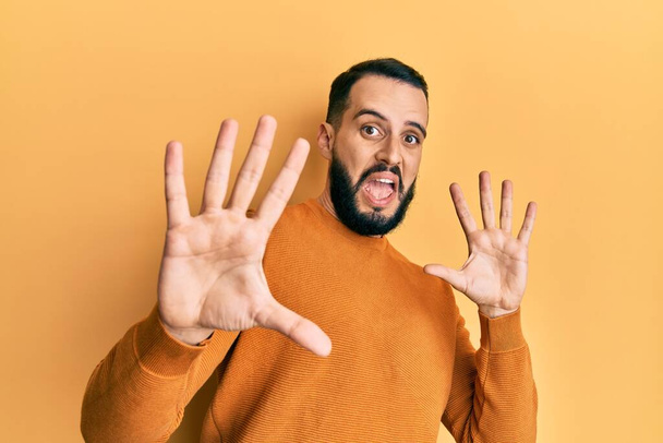 Young man with beard wearing casual winter sweater afraid and terrified with fear expression stop gesture with hands, shouting in shock. panic concept.  - Foto, imagen