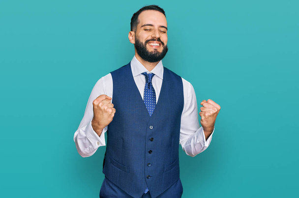 Young man with beard wearing business vest excited for success with arms raised and eyes closed celebrating victory smiling. winner concept.  - Photo, Image