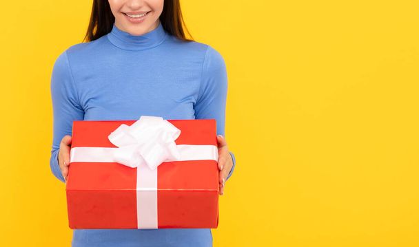 cheerful woman share red present box on yellow background, birthday - Photo, image