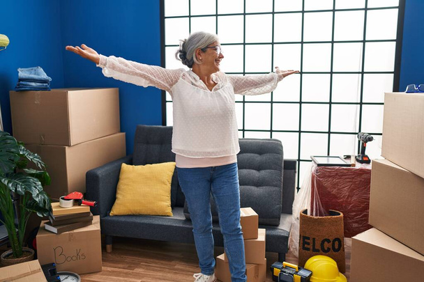 Middle age woman smiling confident with open arms at new home - Photo, Image