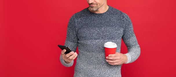 smiling grizzled guy hold phone on red background. hoary man drinking coffee. - Photo, image