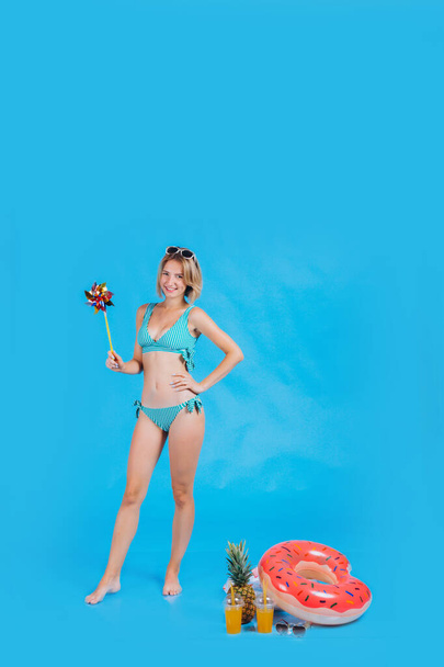 Porträt eines schönen Mädchens im Badeanzug. Mädchen lächelt und trägt Sonnenbrille mit Papierwindrad. Platz für Text. Foto auf blauem Hintergrund. Sommerurlaub am Strand - Foto, Bild