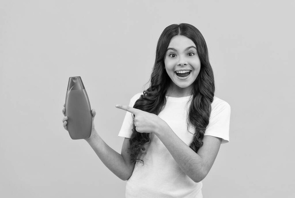 erstaunt teen girl mit langen haaren, die finger auf shampoo-flasche, promotion - Foto, Bild