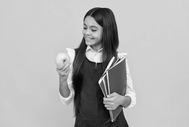 Snacktijd. Gelukkig meisje kijk naar appel met schoolboeken. Een schoolsnack. Voedselonderwijs - Foto, afbeelding