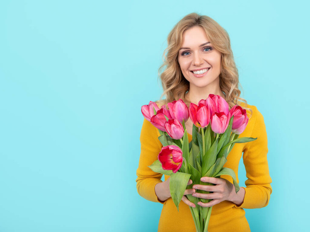 cheerful young woman with spring tulip flowers on blue background - Photo, Image