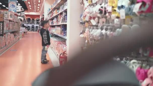 Asian preschooler looking for toys in supermarket while his little brother is in stroller - Filmati, video