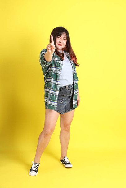 The chubby Asian woman standing on the yellow background with the casual clothes. - Foto, imagen