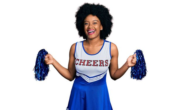 Молодая африканская американка в форме чирлидера, улыбающаяся помпоном и громко смеющаяся, потому что смешная сумасшедшая шутка.  - Фото, изображение