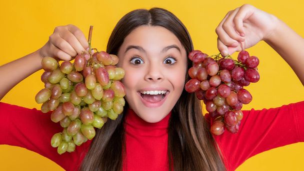 amazed teen girl hold bunch of grapes on yellow background - 写真・画像