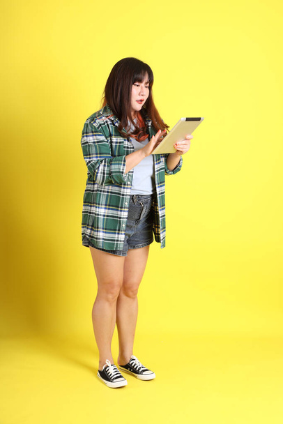The chubby Asian woman standing on the yellow background with the casual clothes. - Foto, Imagen