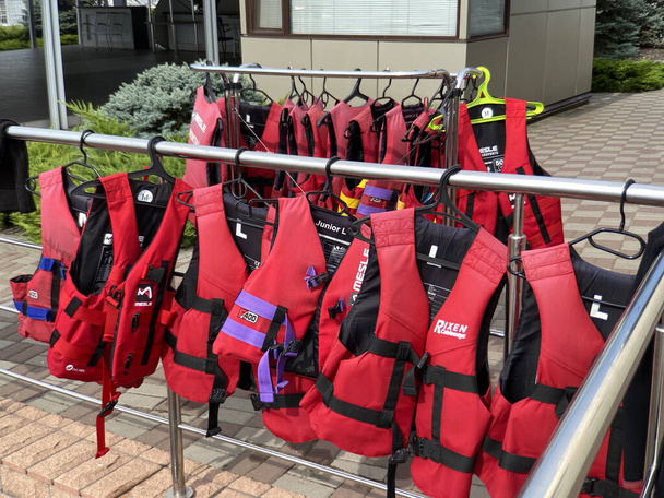 Chalecos salvavidas rojos personales almacenados. Muchos chalecos salvavidas cuelgan en una fila de perchas. Ropa de seguridad protectora en la tienda o tienda de alquiler de barcos, al aire libre - Foto, Imagen