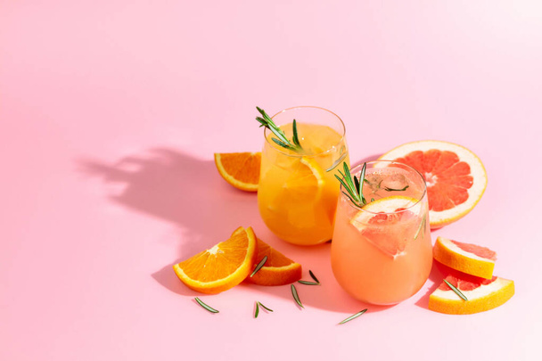 Summer cocktails with grapefruit, orange, rosemary, and ice. Drinks on pink background with copy space. Summer, tropical, fresh cocktail concept. - Фото, изображение