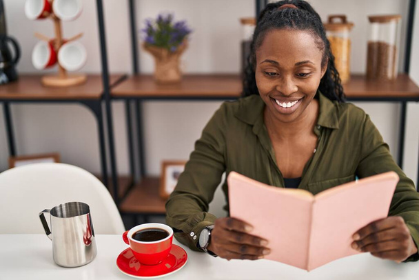 Afrikaans amerikaanse vrouw glimlachen zelfverzekerd lezen boek thuis - Foto, afbeelding