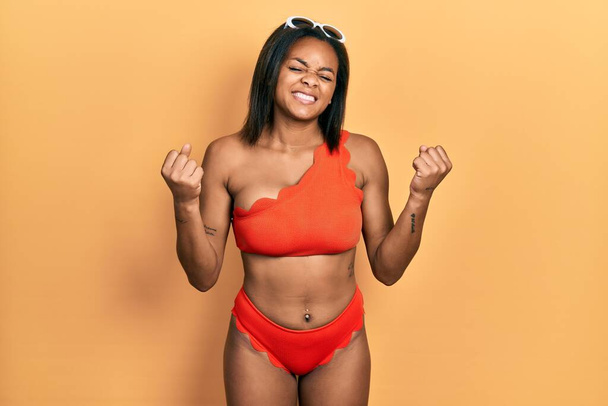 Young african american girl wearing bikini very happy and excited doing winner gesture with arms raised, smiling and screaming for success. celebration concept.  - Фото, изображение