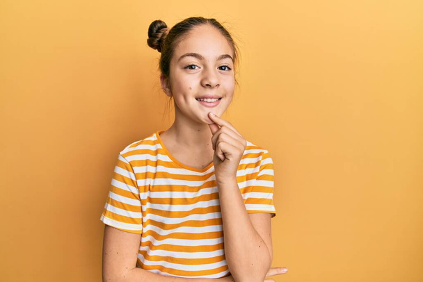 Beautiful brunette little girl wearing casual striped t shirt looking confident at the camera smiling with crossed arms and hand raised on chin. thinking positive.  - Foto, Imagem