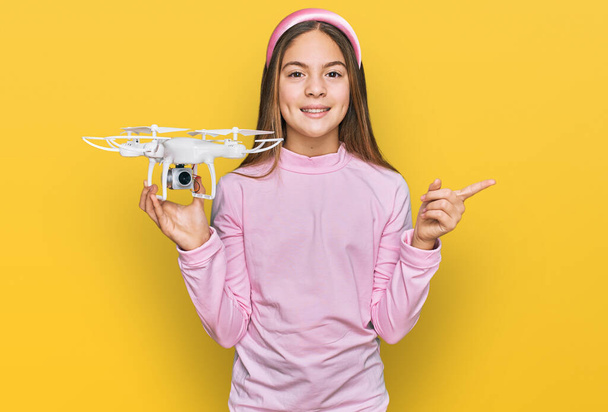 Beautiful brunette little girl using drone smiling happy pointing with hand and finger to the side  - Foto, immagini